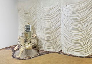 Mixed-media installation including fabric, photographs, clothing, found objects, mementoes, mirrors, found furniture, sand, dried petals, candles, laser prints on wall, pearls and found images