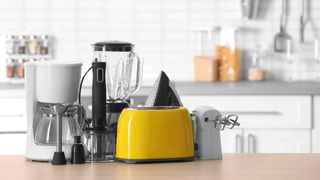 A selection of appliances on a kitchen counter including a toaster, coffee maker, blender, immersion blender, steam iron and hand mixer