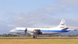 A white plane is seen on a runway. It has a NASA sign on its tail.