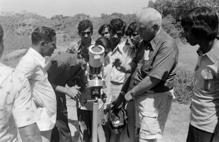 A group of men gather around a small telescope pointing at the sun to view the solar eclipse.