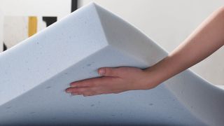 Linenspa vs Lucid mattress toppers: A person holds up the Lucid 4" Gel Memory Foam Mattress Topper by one corner to show how thick it is