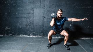 Man performing a dumbbell push press with dumbbell on his shoulder in a squat position