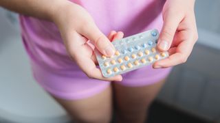 A young woman holds a packet of birth control pills