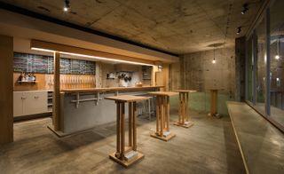 A view to the bar behind three wooden tables. Exposed concrete floor and walls