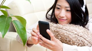 A woman laying down, using her phone and wearing headphones