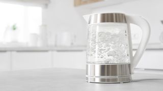 Water boils inside a chrome and clear electric kettle placed on a white countertop