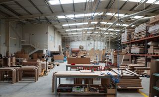 Interior view of the Gual manufacturing house featuring light coloured walls, grey floors, large shelving units, lots of wood and workstations