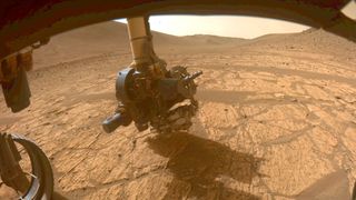 a mars rover&#039;s robotic arm investigates a bright, dusty rock on the red planet