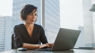 Woman sitting at a table in a modern corporate office, working at a laptop