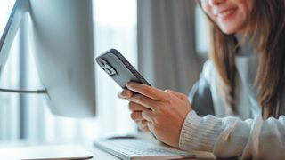 A woman sitting at a table, holding her phone and smiling while looking at it