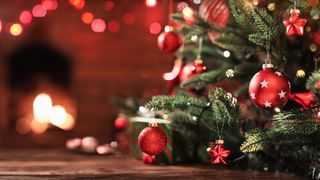 Close up of a Christmas tree with red decorations and a fire place in the background