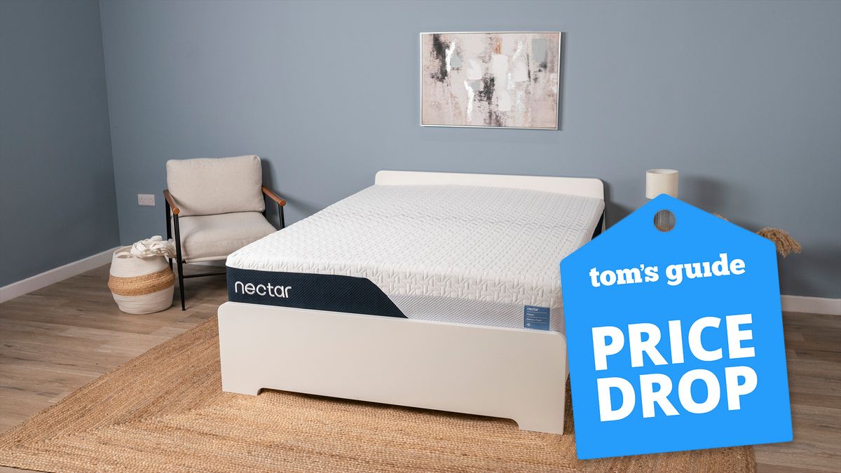 Image shows the Nectar Classic Mattress placed on a white wooden bedframe in a blue-coloured room with a blue price drop sales badge overlaid on the image