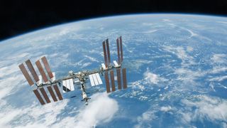 a T-shaped space station with multiple solar arrays floats above earth