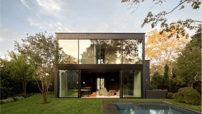 a sag harbor house with glazed facade and open curtains looking towards garden and swimming pool