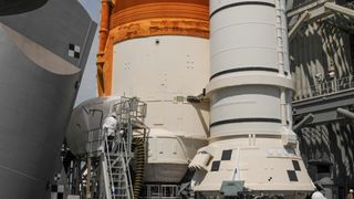 The bottom of the Artemis 1 moon rocket with technicians working on its fuel lines