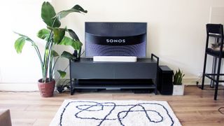 the sonos beam gen 2 soundbar in white pictured beneath a tv on a black cabinet