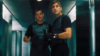 Matt Damon looking nervous while standing behind George Clooney who also looks nervous and is holding a remote.