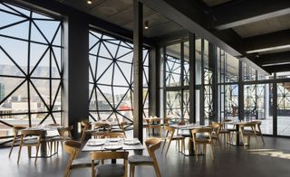 Dinner table setup with 4 seating per table with a mix of dark grey leather and oak wood chairs and square tables dressed with plates and and glasses