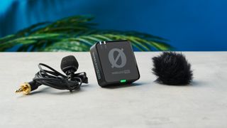 The Rode Wireless Pro microphone and its lav mics standing on a stone surface with a blue wall in the background