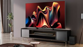 Hisense U7N TV on a wooden media unit in front of a beige wall. On screen is a wavy graphic in red and yellow with a touch of blue.