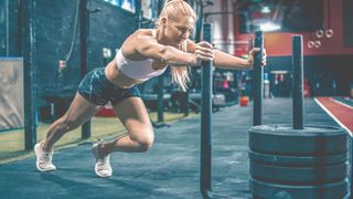 Woman performing a sled push in the gym with arms extended and left leg forward