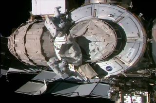 NASA astronauts Bob Behnken (at bottom) and Chris Cassidy remove a pressurized mating adapter cover from the end cone of the Tranquility node in preparation for the addition of Nanoracks' commercial airlock during a July 21, 2020 spacewalk outside the International Space Station.