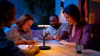 Philips Hue Go portable - fire mennesker sidder udenfor omkring et bord ved aftentid med en Philips Hue Go portable på bordet