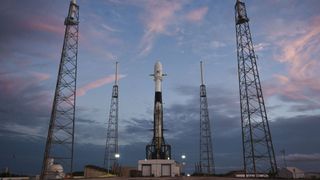 Falcon 9 rocket on launch pad surrounded by blue skies and wispy pink cloudss