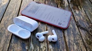AirPods Pro 2 earbuds next to their charging case and an iPhone
