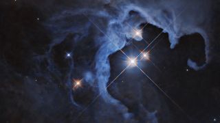 A spooky view of a deep blue cloud. In a cavity within the cloud, there are a few solitary sparkling stars.