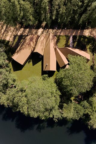 the lake house, a timber structure in a forest, made up of a cluster of volumes with pitched roofs