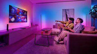 Two gamers on a sofa enjoying a split screen racing game on a TV lit by the Philips Hue Play HDMI sync box 8K.