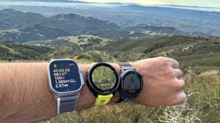 The Apple Watch Ultra 2, Garmin Forerunner 965, and COROS PACE 3 all worn on one wrist on the Mount Diablo Summit Trail, overlooking the valley below.