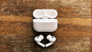 AirPods Pro 2 buds pictured next to their charging case on a wooden surface