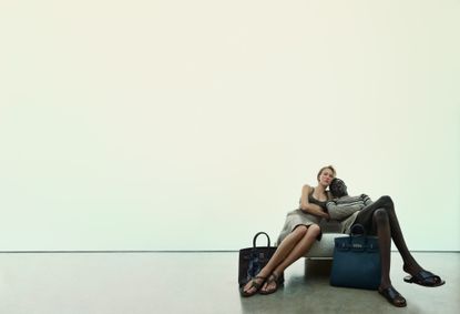 Male and female model sat on chair with two Hermès travel bags 