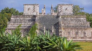 A large stone pyramid with plants in the foreground.