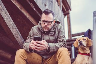 Hiker sitting on the stairs of hikers rest cabin with a dog and using smart phone.