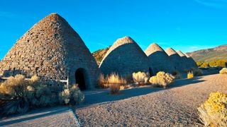 A row of stone huts with roofs tapering to a point with blue sky behind.