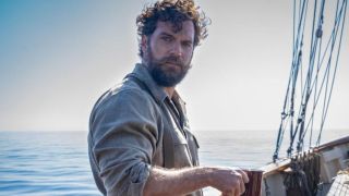 Henry Cavill looking stoic while standing on a boat deck with a cup of coffee in The Ministry of Ungentlemanly Warfare.