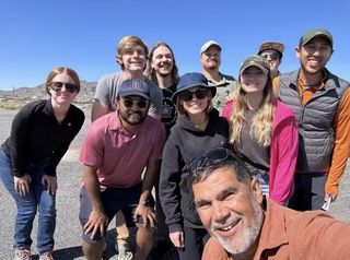 a group of people in various casual hiking attire smiles while outdoors.