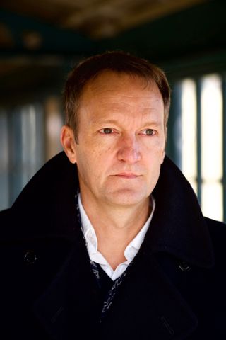 closeup of a serious-faced man wearing a dark coat with big lapels