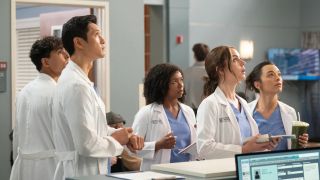 Some of the cast, wearing scrubs and white coats, look up with concern in &quot;Grey&#039;s Anatomy&quot; season 20