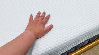 A hand touching the cover of the Emma Luxe mattress