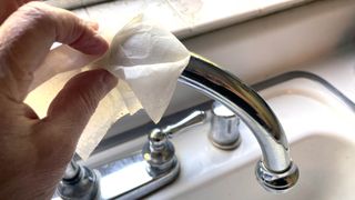 Someone polishing a chrome faucet with a dryer sheet