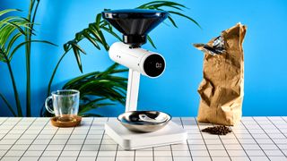 the acaia orion coffee bean doser is a white sci-fi-inspired bean doser with a rotating dial and LED screen and a bean hopper photographed against a blue tom's guide background