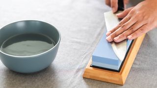 A knife being sharpened on a whetstone next to a bowl of water