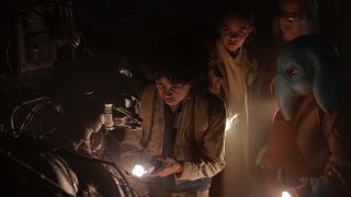 Image from the TV show Star Wars: Skeleton Crew. A group of four children are each shining a torch, inspecting a broken-down robot in front of them.