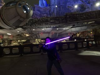 Christine Chan holds her violet lightsaber in front of the Millennium Falcon