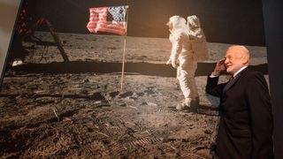 Buzz Aldrin, second man on the moon salutes an image of himself standing on the moon next to the American flag.