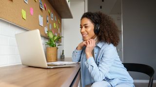 A young woman sitting at a desk with a laptop and using headphones